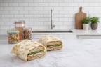 Sandwich wrapped in a honeycomb patterned wrap on a marble surface with jars in the background.
