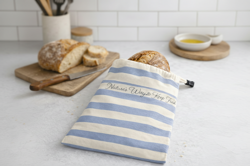 Striped bread bag with text on a kitchen counter with bread and utensils.