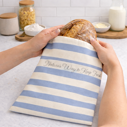 Person holding a loaf of bread in a blue and white striped bag with text on a kitchen counter.